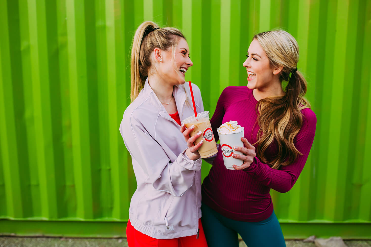 Two smiling women holding coffee in front of a green background