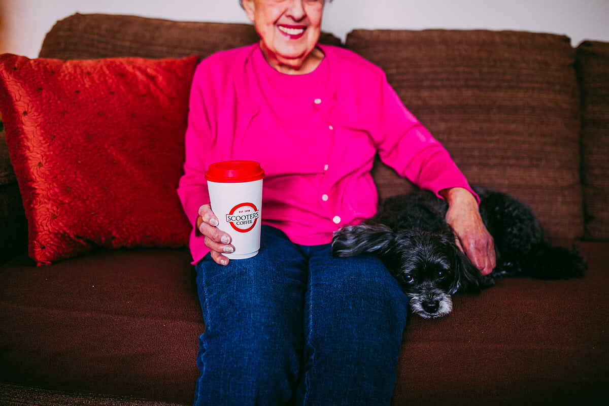 Woman holding coffee cup sitting on couch with a dog