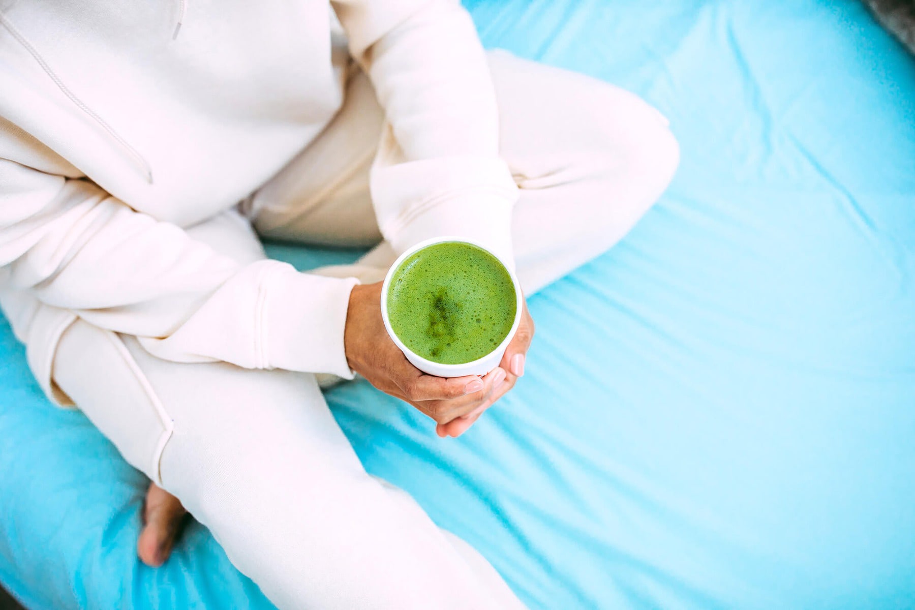 Woman sitting on blue bed holding matcha latte