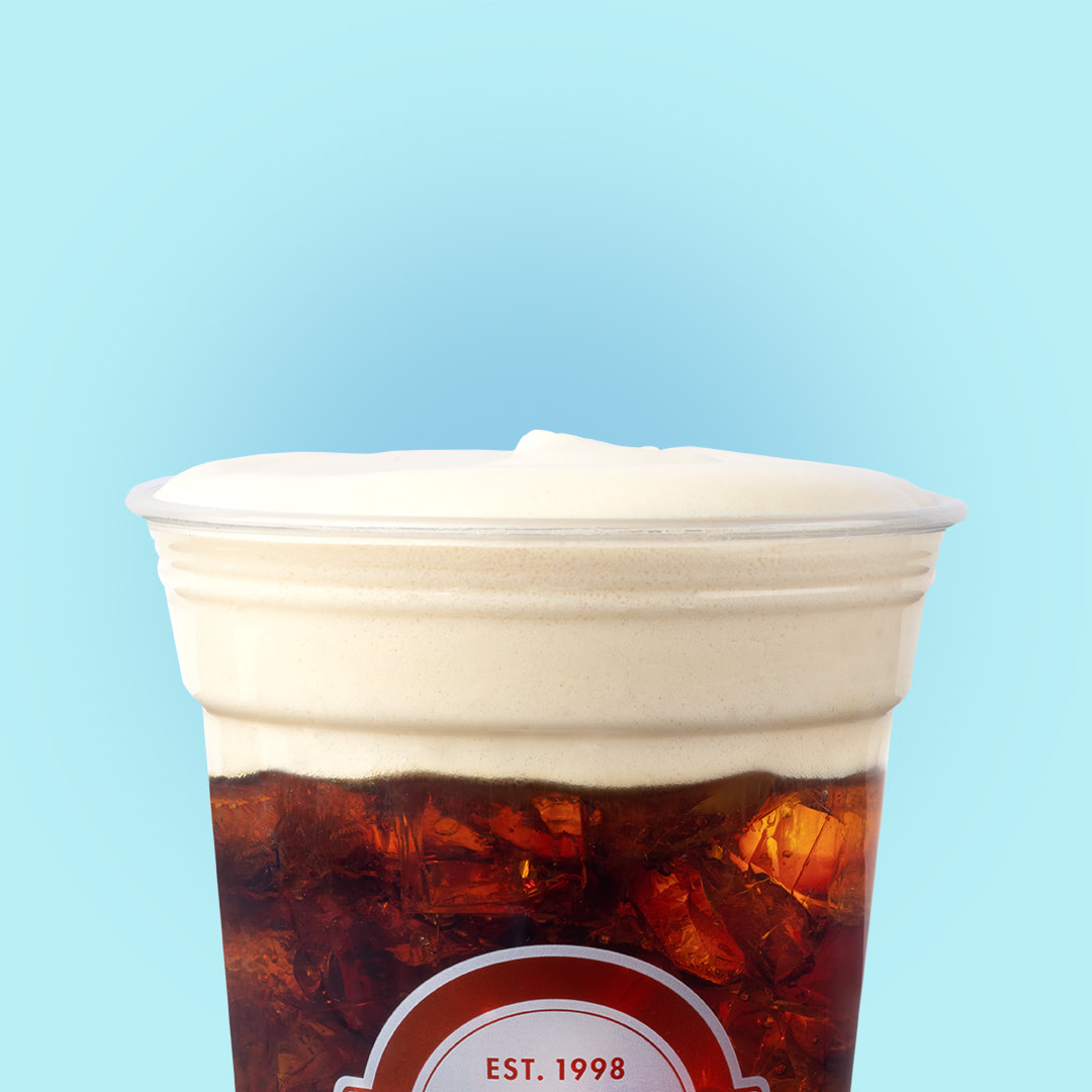 Iced coffee topped with cold foam on blue background