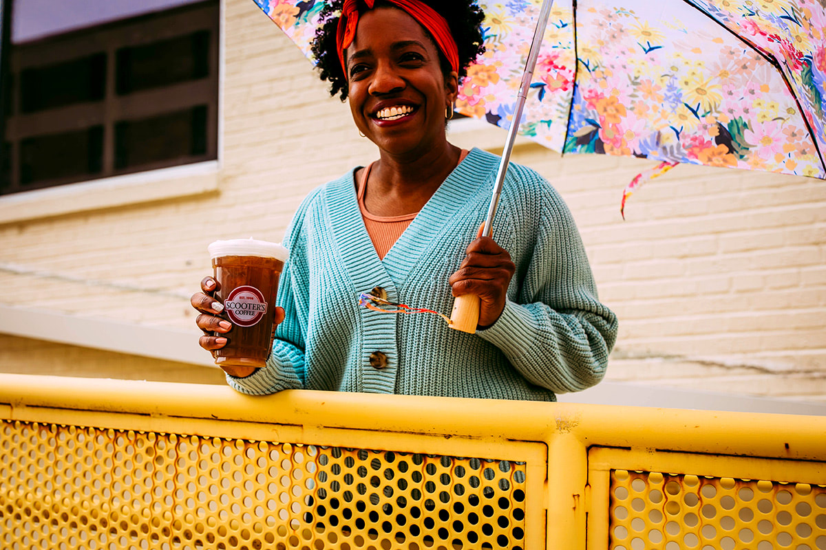 Smiling woman holding umbrella and coffee